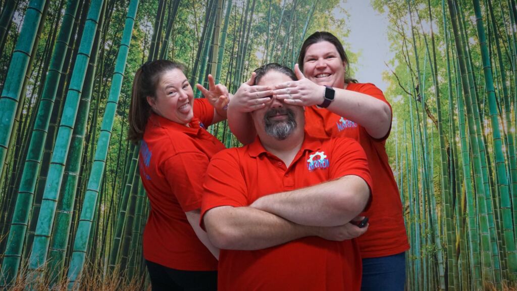 The Narrow Escape Rooms Penrith owners in front of a bamboo forest poster smiling at being cheeky.